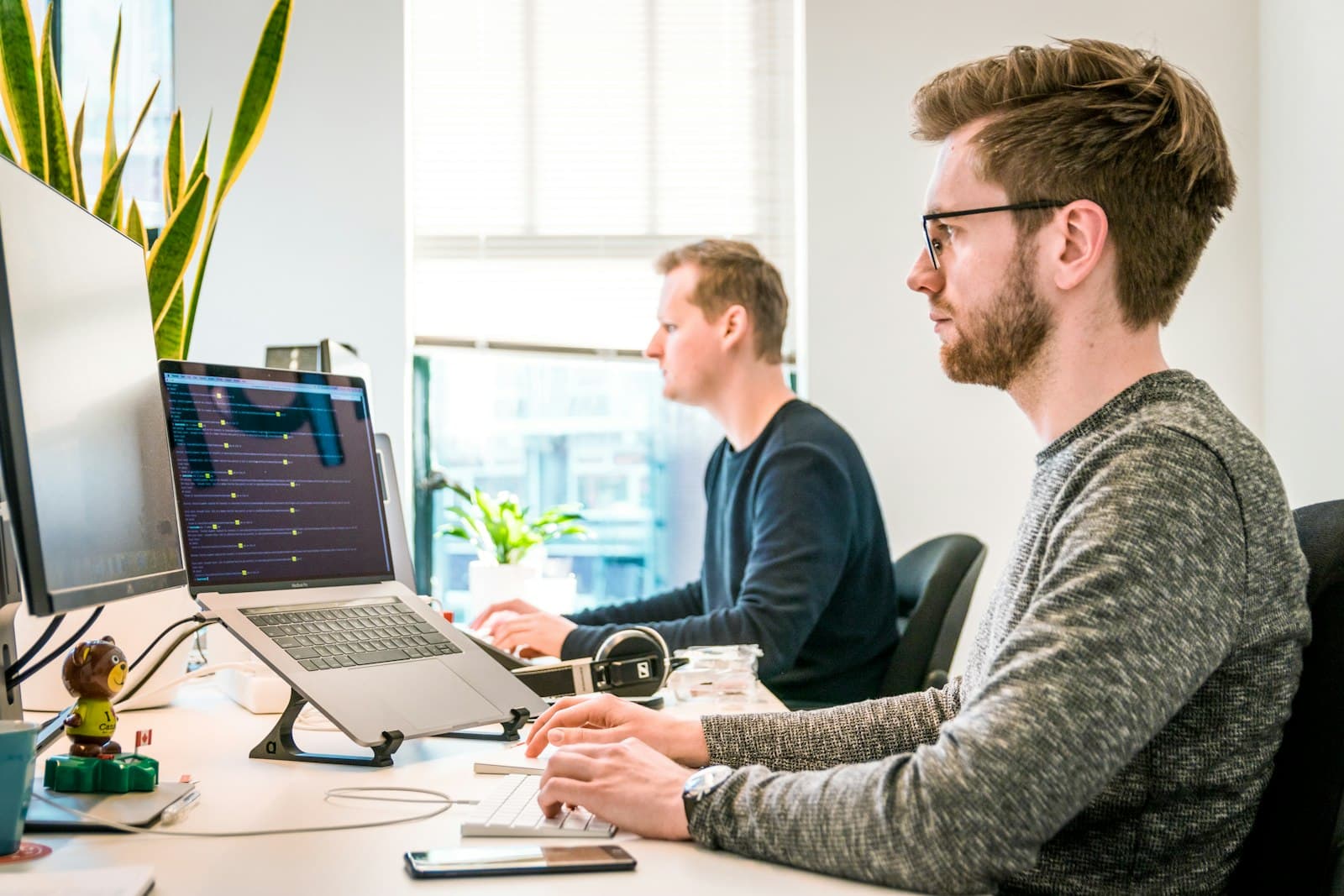 Two engineers working at desks with code on their screens